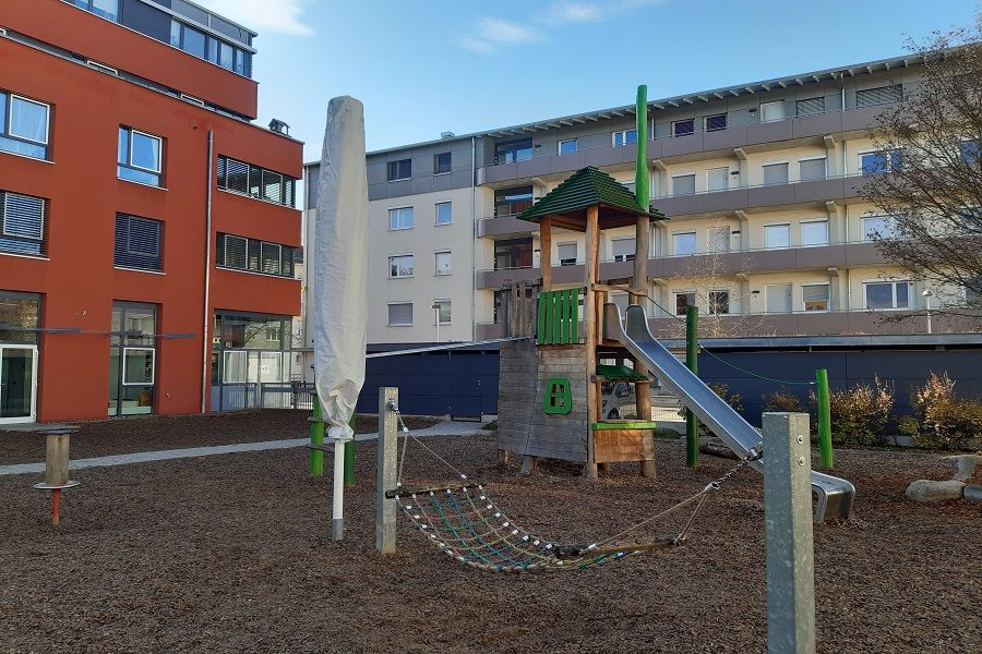 Rote Außenfassade und Garten mit Hängematte und Rutsche des Kinderhauses Janusz Korczak